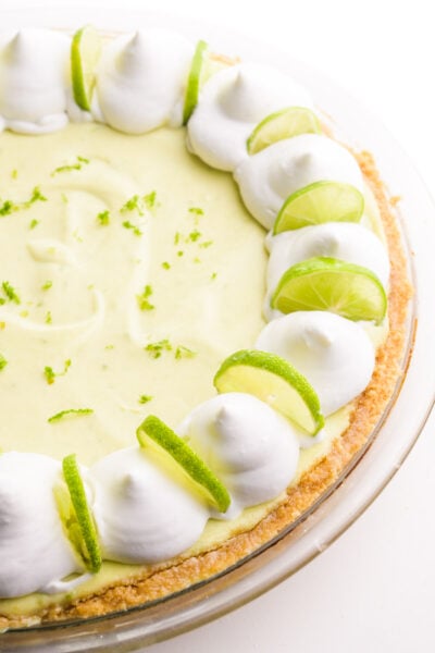 Looking down on a whole key lime pie with whipped cream dollops and lime slices around the edges.