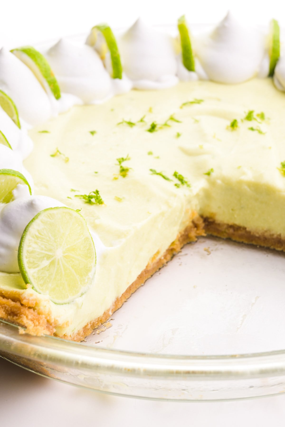 A key lime pie has several slices cut out, revealing the crust and filling. There's whipped cream and lime slices on top of the pie.