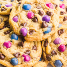 Looking down on a plate full of vegan M&M cookies, showing colorful candy pieces and chocolate chips in each cookie.