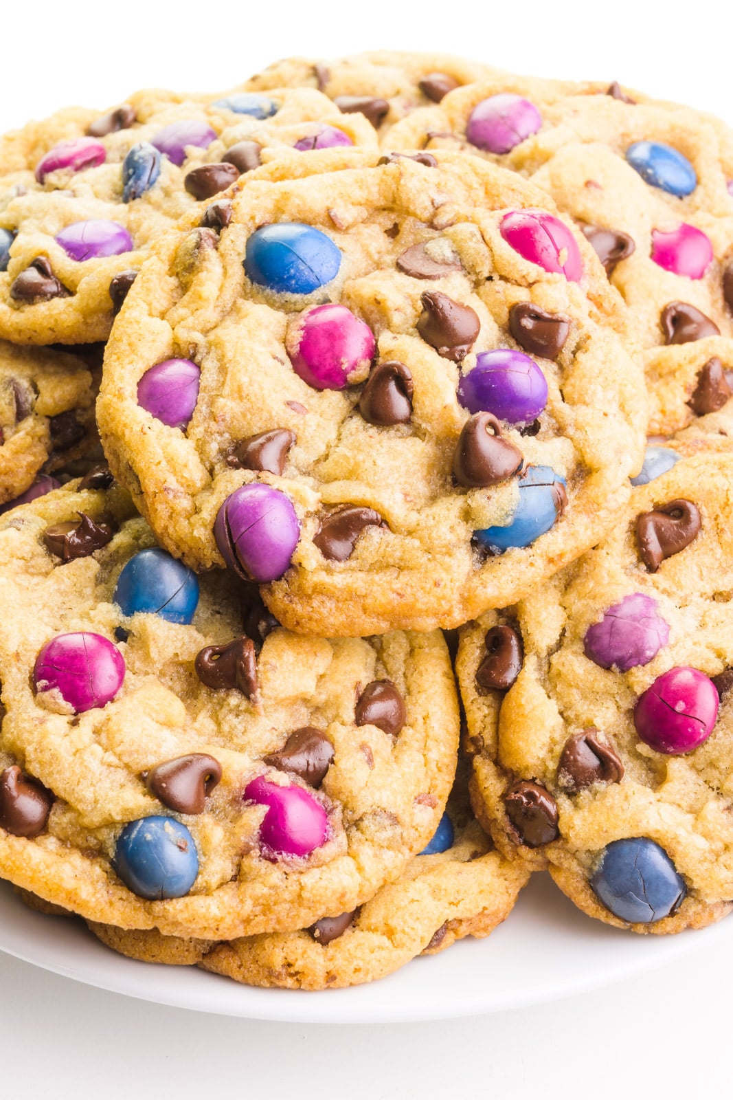 Looking down on a plate full of vegan M&M cookies, showing colorful candy pieces and chocolate chips in each cookie.