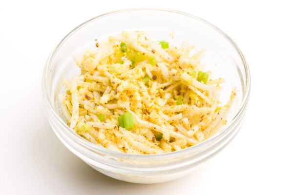 Looking down on a bowl full of vegan mozzarella, parmesan, and chopped green onions.