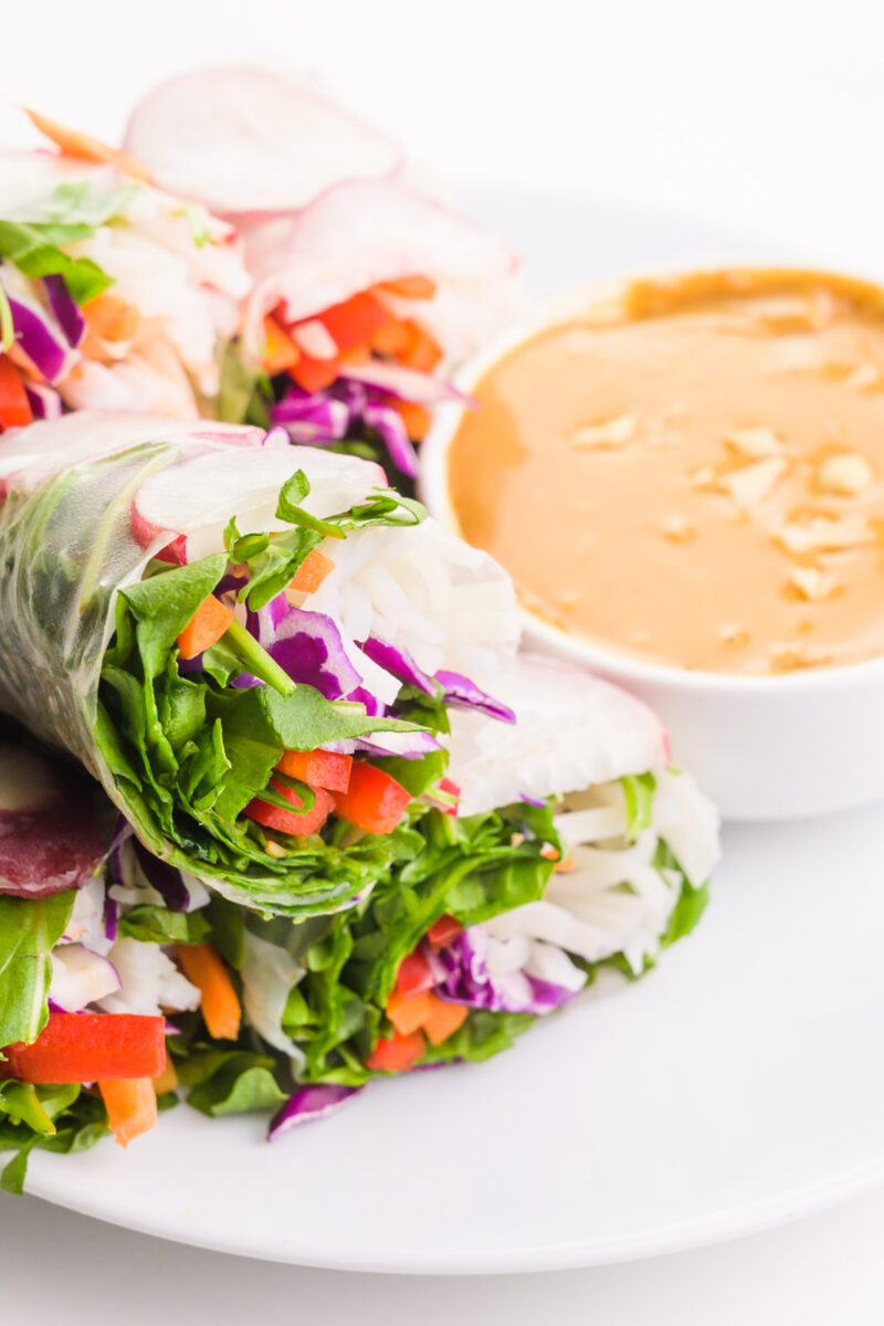 Vegan spring rolls are on a plate sitting next to peanut sauce.