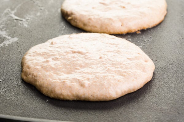 Pancakes are cooking on a griddle, waiting to be flipped.