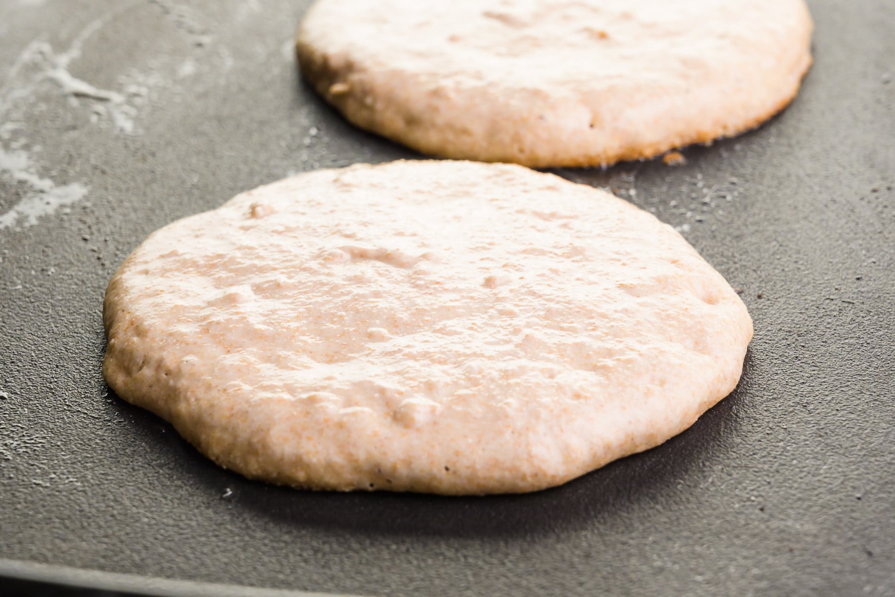 Pancakes are cooking on a griddle, waiting to be flipped.