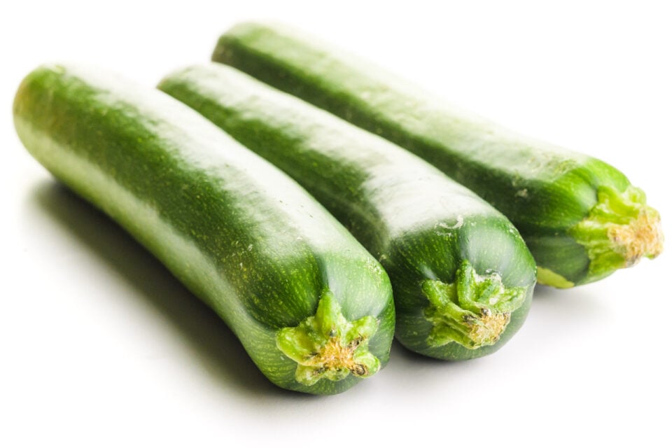 Three zucchinis sit side-by-side on a white table.