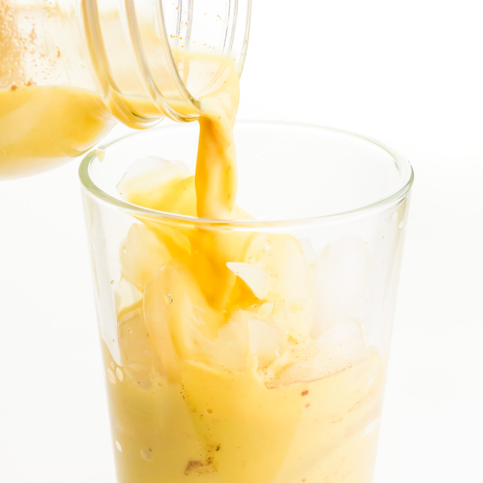 Golden milk is being poured into a glass with ice.