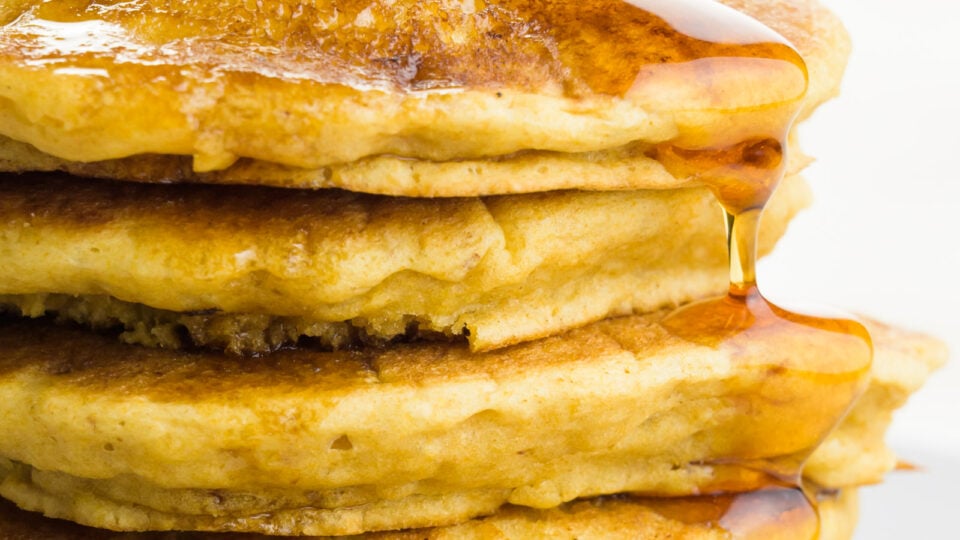 A close-up photo of a tall stack of pancakes, showing maple syrup following over the edges.