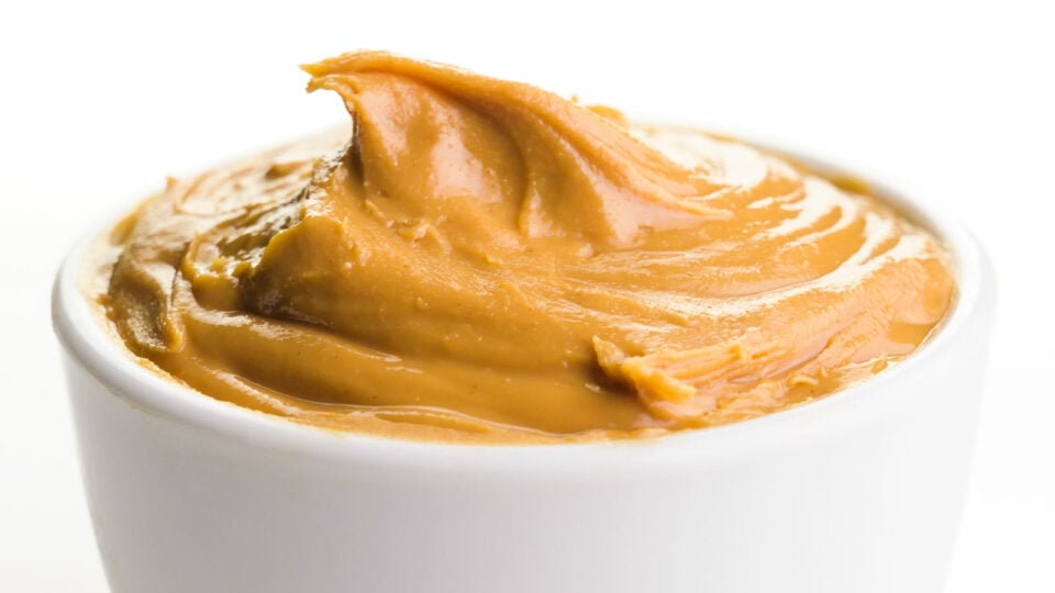 A small, white bowl holds creamy peanut butter inside.