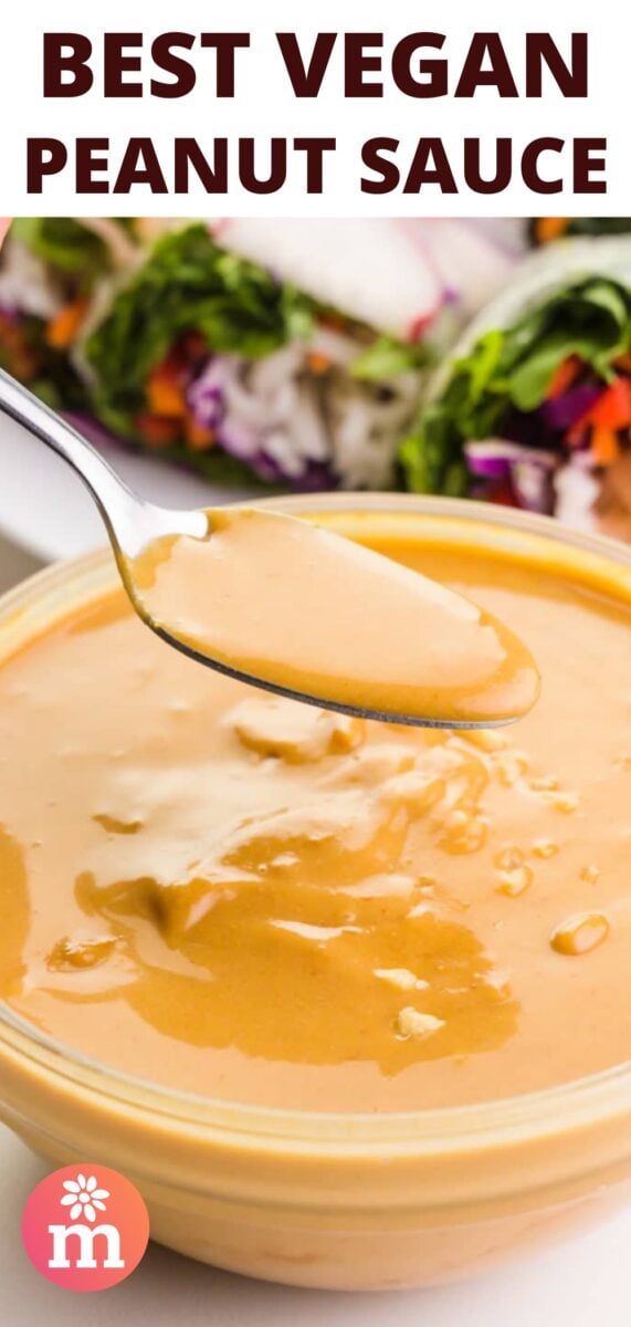 A spoon full of peanut sauce hovers over a bowl full of of it. There are spring rolls in the background ready for dipping in the sauce. The text at the top of the image reads, Best Vegan Peanut Sauce.