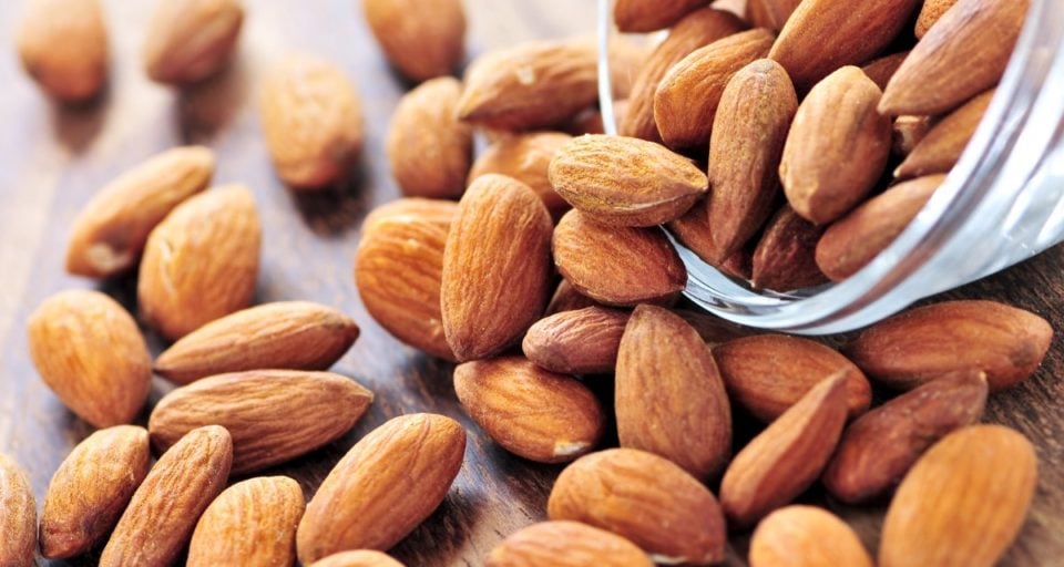 Raw almonds are being poured onto a wood cutting board.
