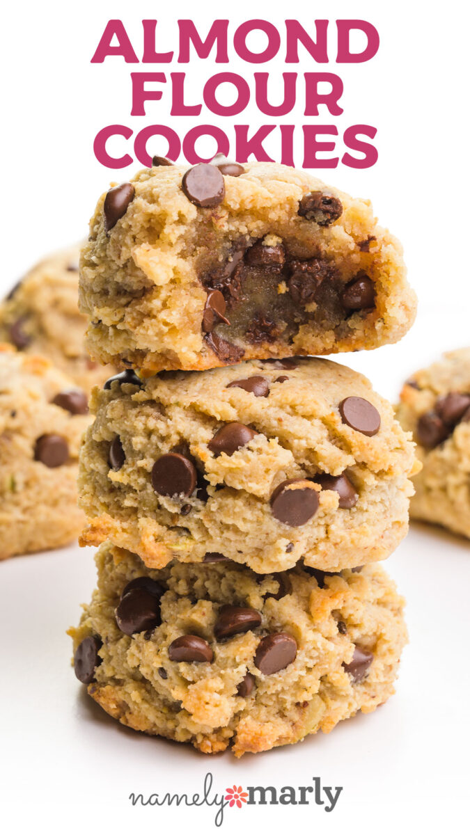 A bite has been taken out of an almond flour cookie, showing lots of chocolate chips inside. It's the top cookie of a stack of three. Text reads "Almond Flour Cookies namelymarly.com"