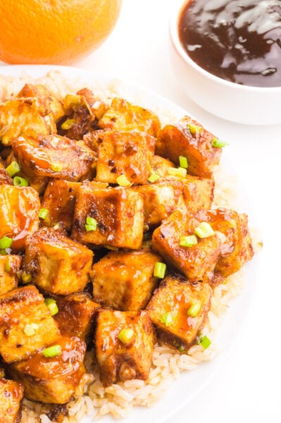 Looking down on a plate of orange tofu on a bed of rice.