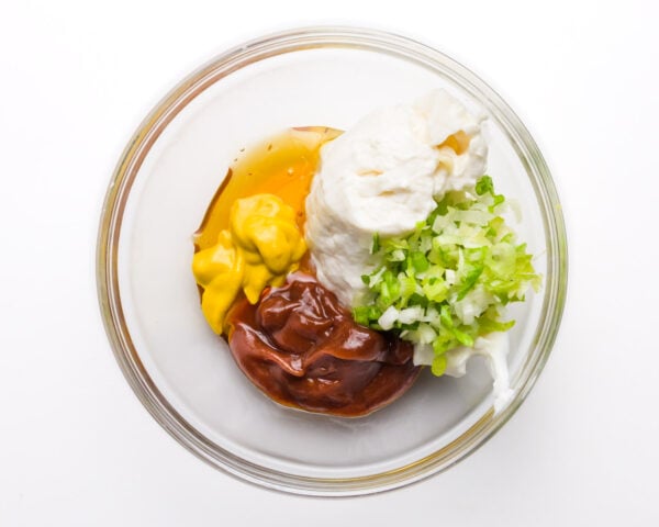 Ingredients are in a glass bowl, including syrup, chopped green onions, vegan mayo, bbq sauce, and more.