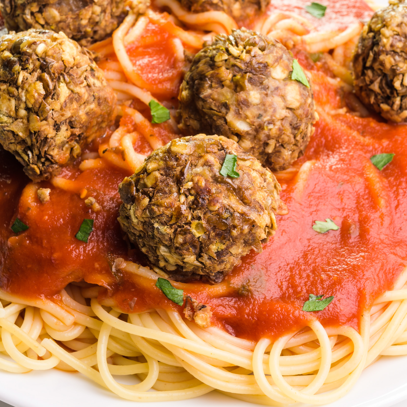 Lentil meatballs sit on top of red sauce and spaghetti on a plate.