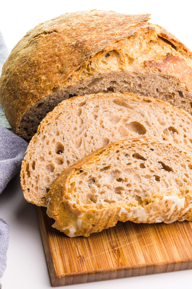 A loaf of whole wheat bread sits on a cutting board with a couple slices sitting in front of it.