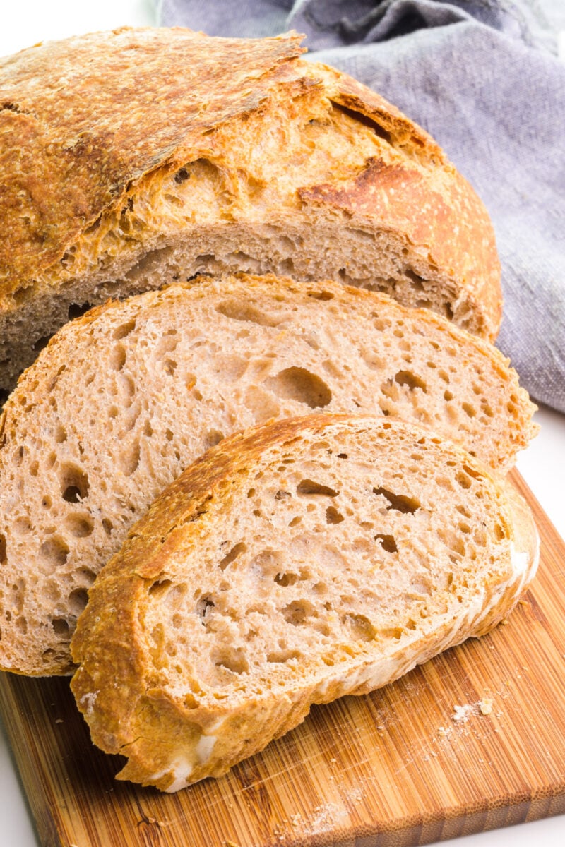 A close-up of whole wheat no-knead bread on a cutting board with a few slices in front.