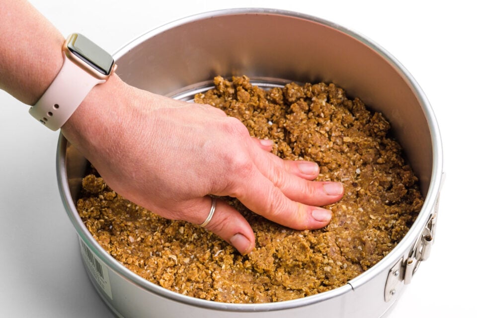 A hand presses crust into the bottom of a springform pan.