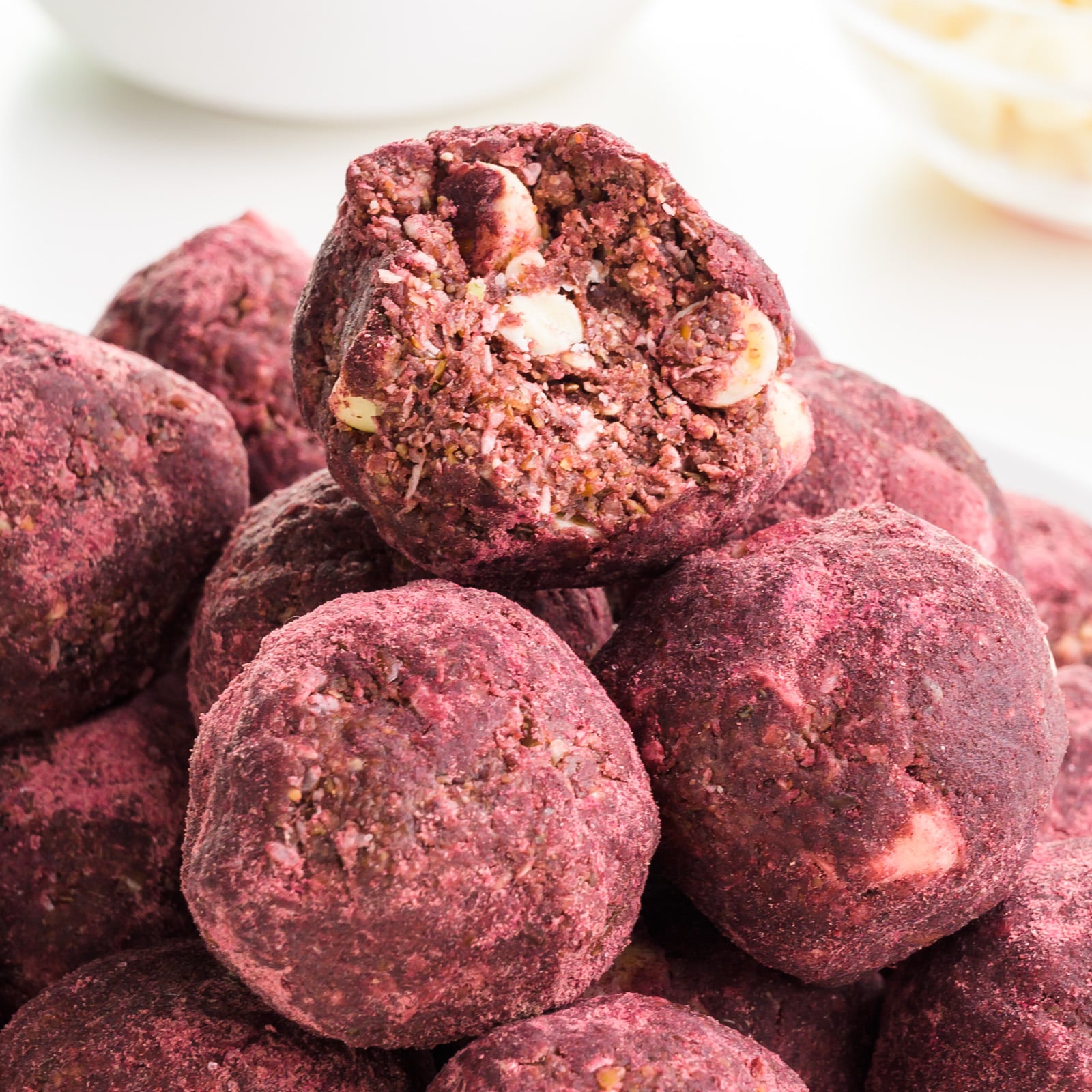 A red velvet ball has a bite taken out of it showing white chocolate chips inside. It sits on a stack of more of the energy balls.