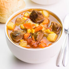 Looking down on a bowl of vegan beef stew sitting beside spoons and dinner rolls.