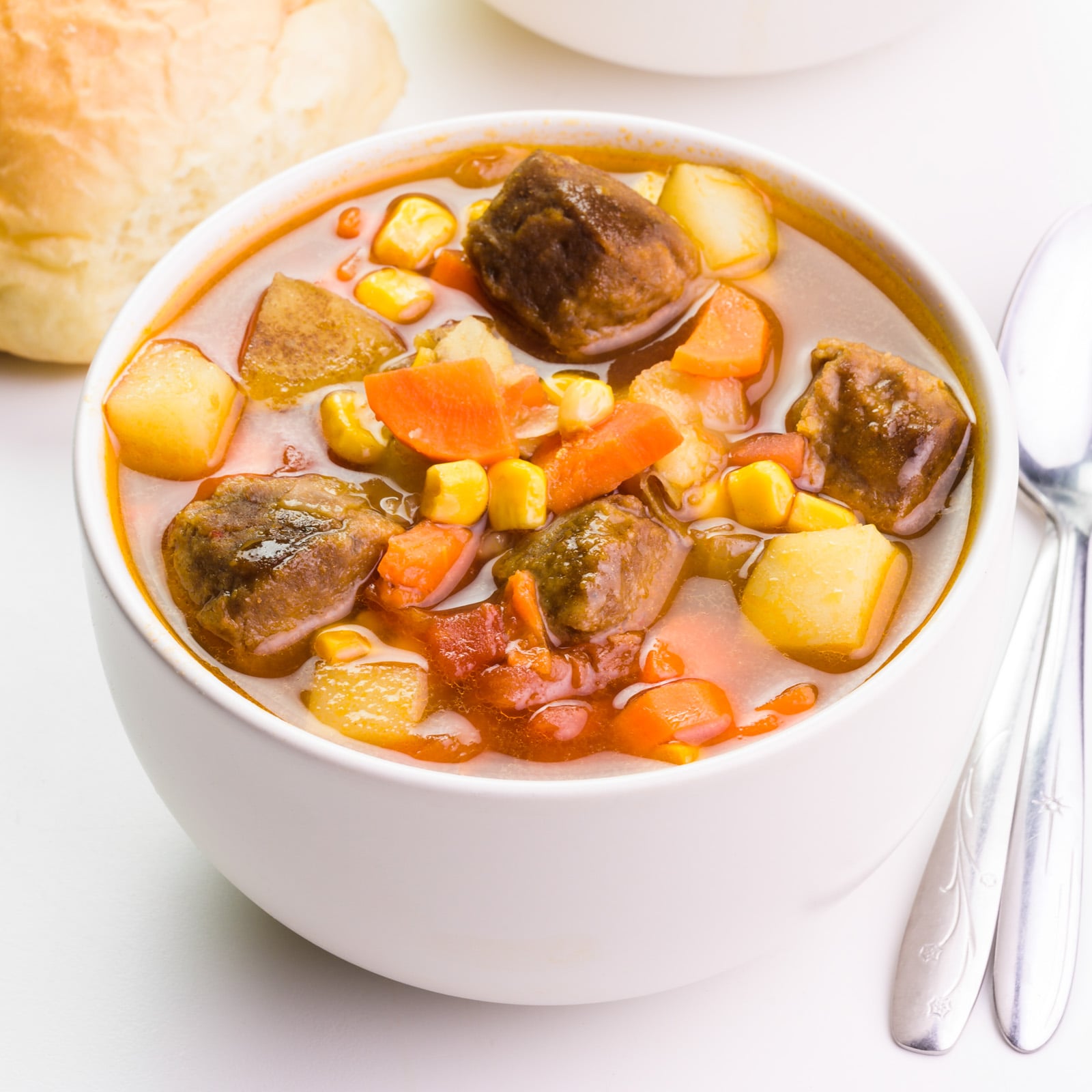 Looking down on a bowl of vegan beef stew sitting beside spoons and dinner rolls.