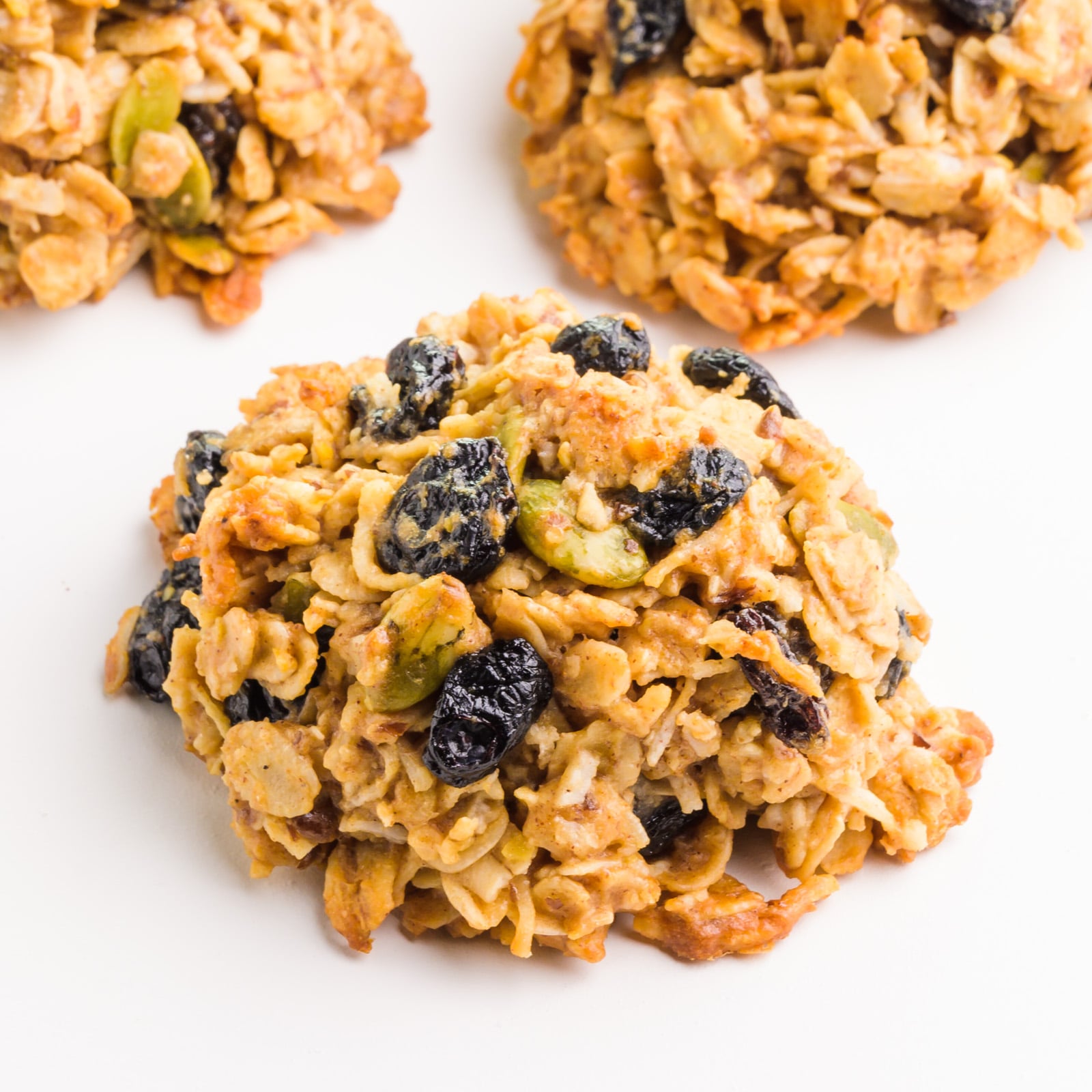 A breakfast cookie sits on a white counter, with several cookies around it.
