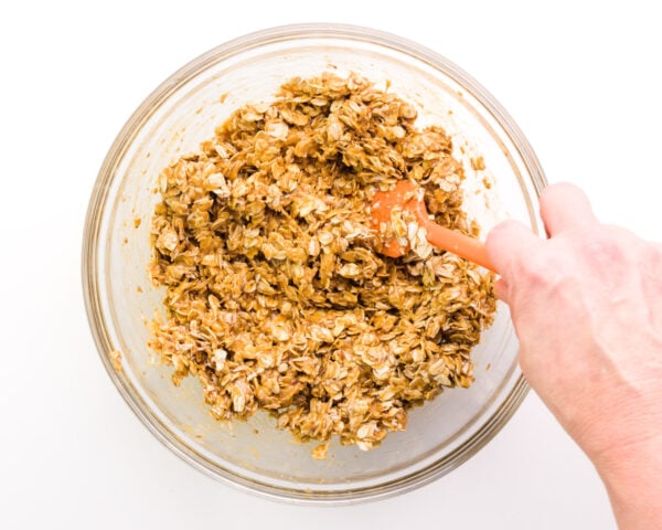 A hand holds a spatula, stirring cookie dough together.