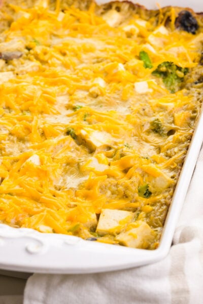 Tofu casserole is in a white baking dish. It has vegan cheddar cheese melted on top.