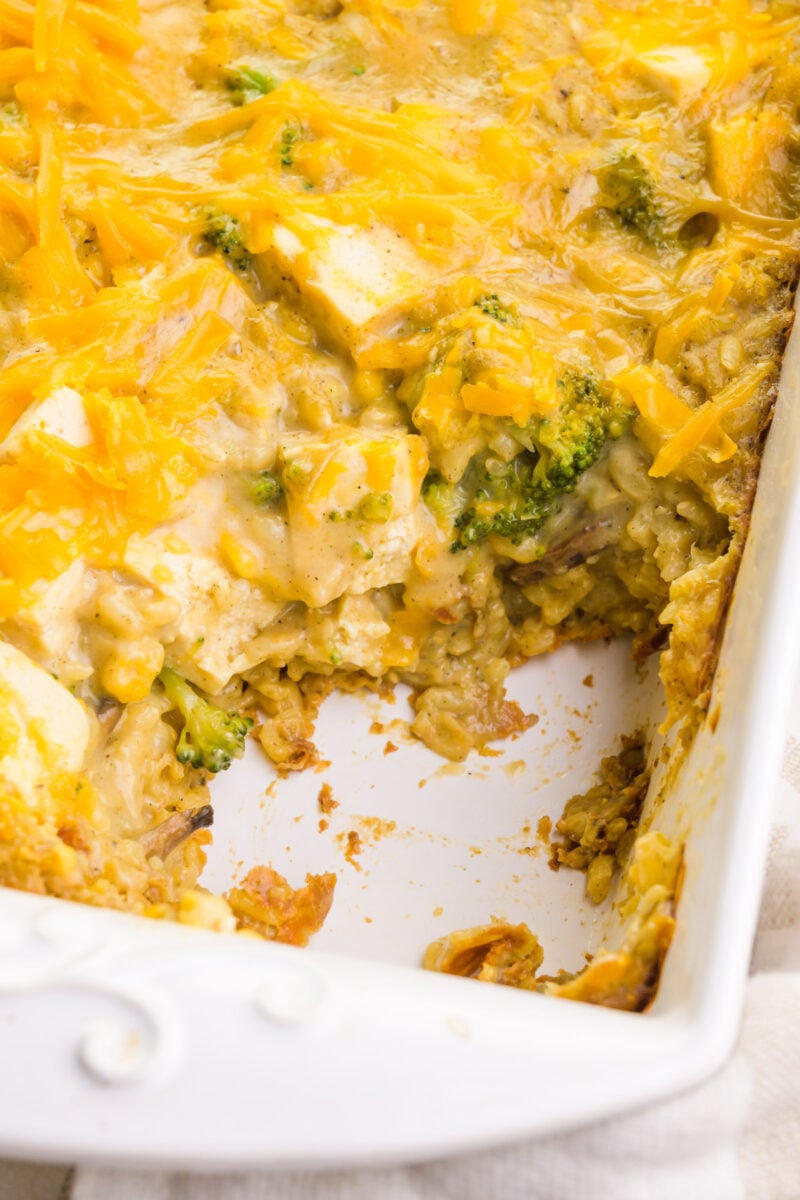 Looking down on a casserole with some of it spooned out. It shows bits of rice, broccoli, and tofu cubes in a cheesy casserole mixture.