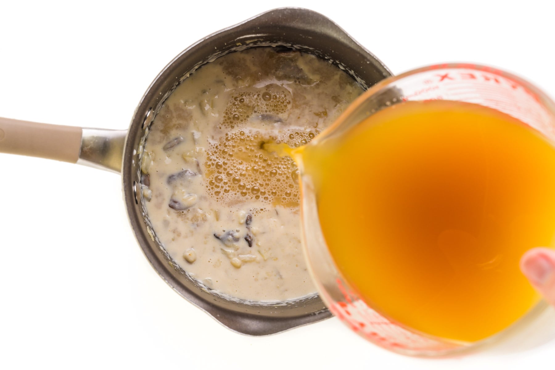 Vegetable broth is being poured into a saucepan with a thickened mushroom mixture.