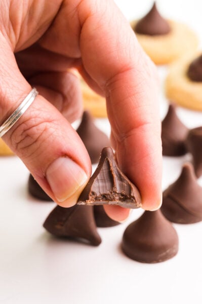 A hand holds a vegan chocolate kiss with a bite taken out. There are more of the candies and cookies in the background.