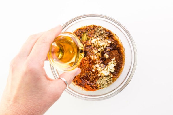 A hand holds a bowl of syrup, pouring it into a bowl with other sauce ingredients.