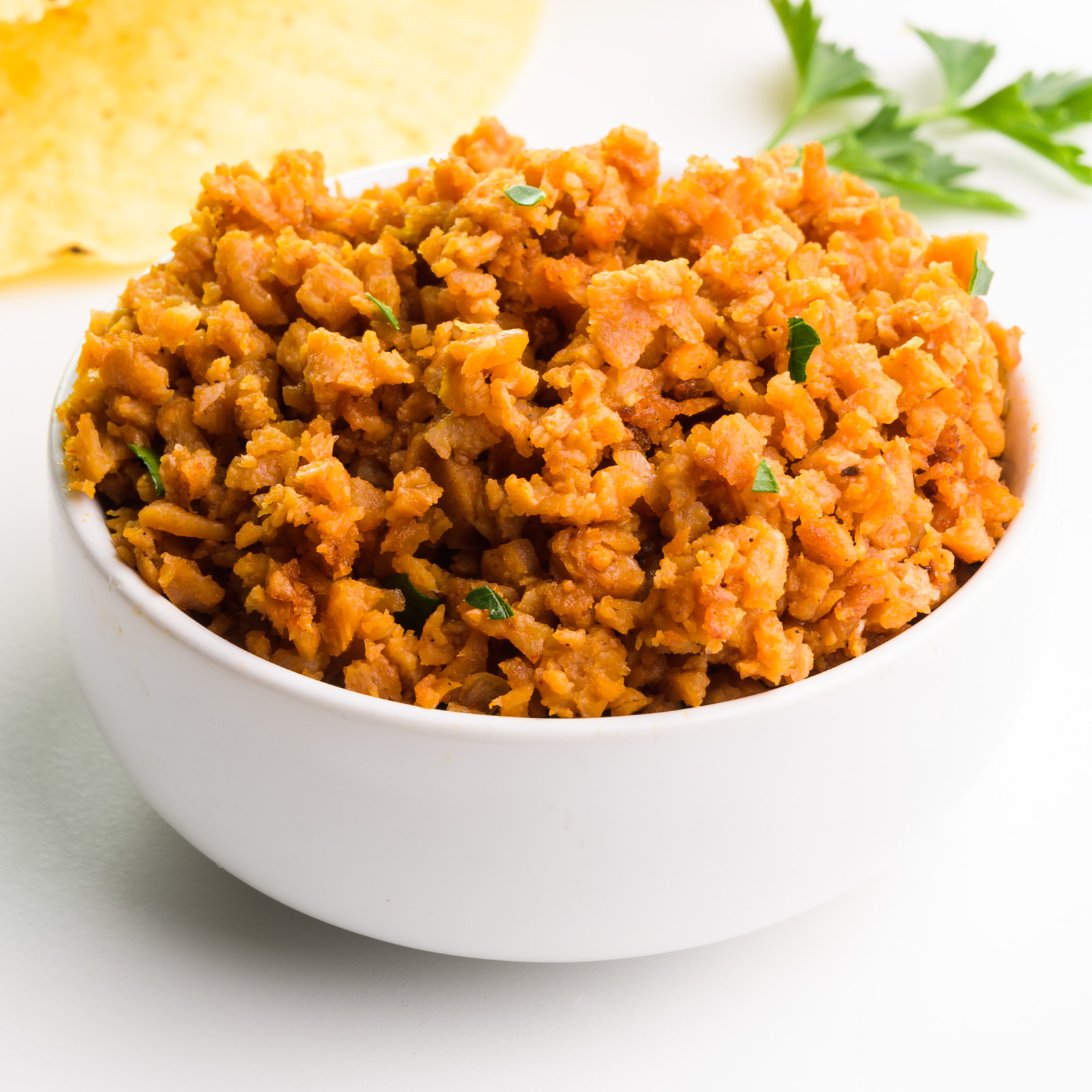 A bowl of veggie crumbles sits in front of taco shells and fresh herbs.