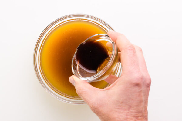A hand holds a bowl with sauce, pouring it into another bowl with vegetable broth.