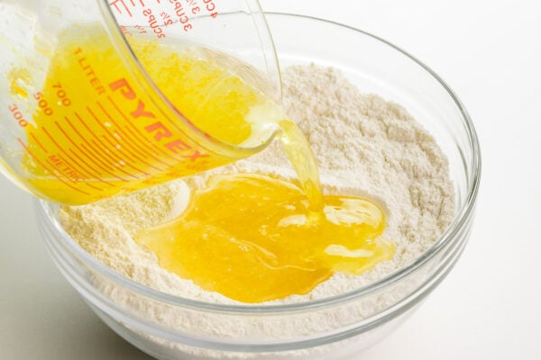 A lemon liquid mixture is being poured into a bowl with a flour mixture.