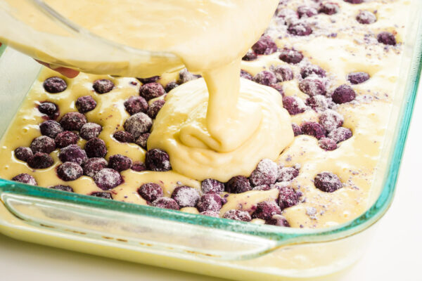 Batter is being poured over a lemon cake batter with blueberries on top.