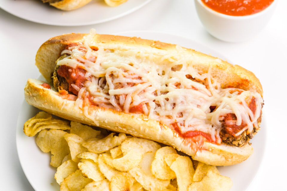 Looking down at a lentil meatball sub sandwich sitting on a plate with potato chips.