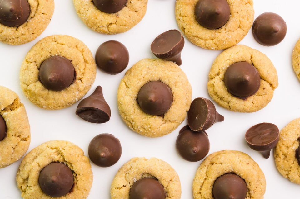 Looking down on several peanut butter cookies with chocolate kisses on top. There are several of the vegan kisses candies around the cookies.