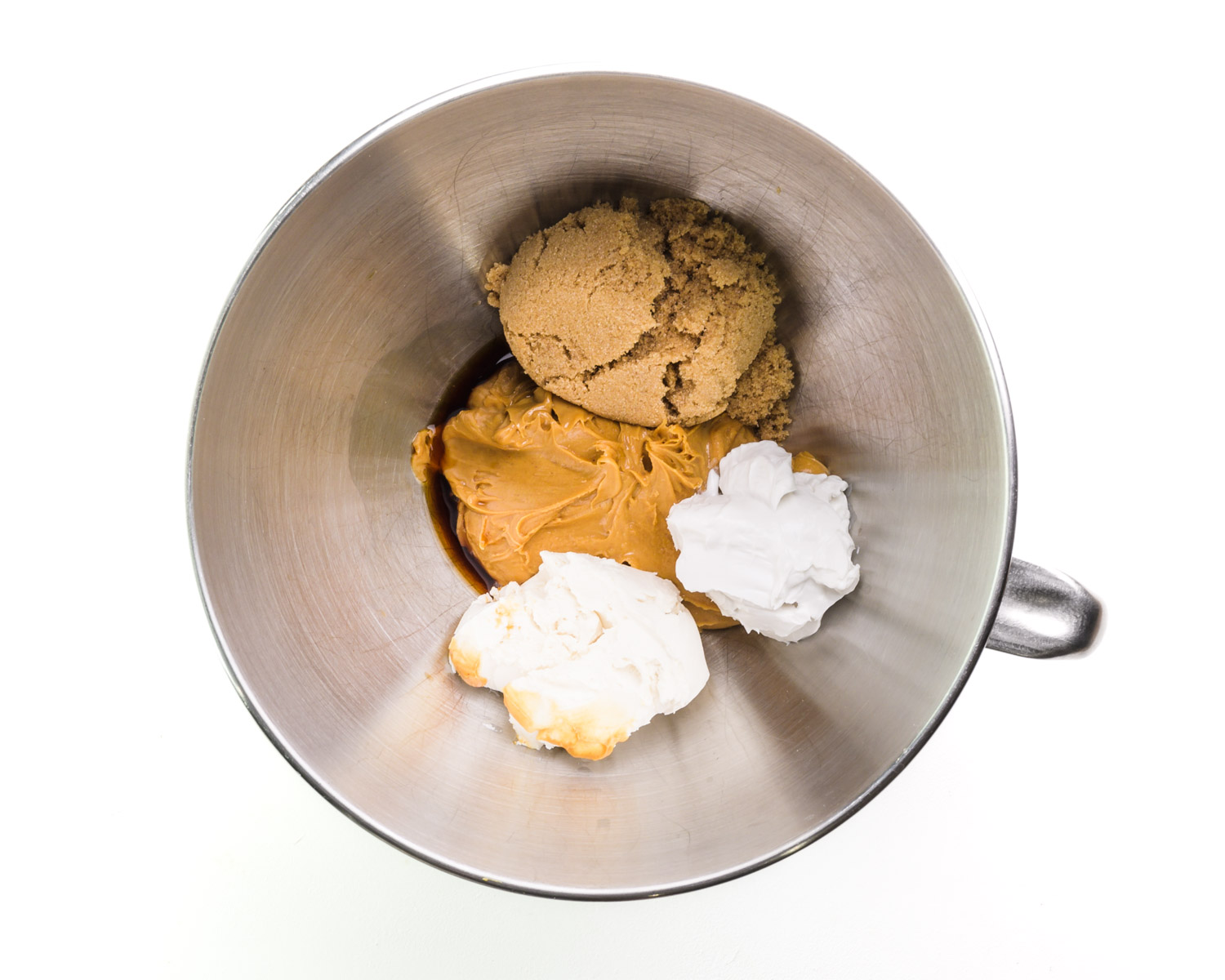 Ingredients are in the bottom of a mixing bowl, including peanut butter, brown sugar, and coconut fat.