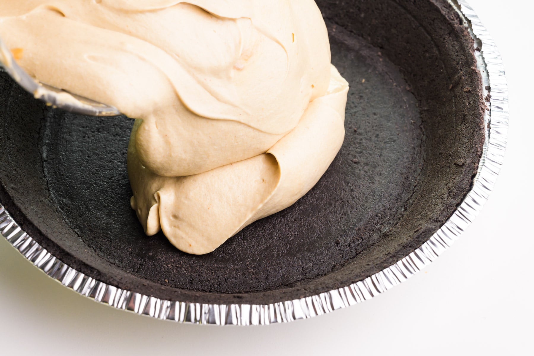 Whipped peanut butter pie filling is being added to an oreo pie crust.