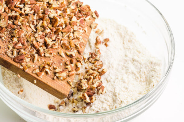 Chopped pecans are being poured from a cutting board into a bowl with a flour mixture.