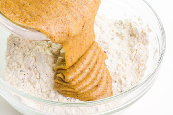 A golden butter mixture is being poured into a bowl with a flour mixture.