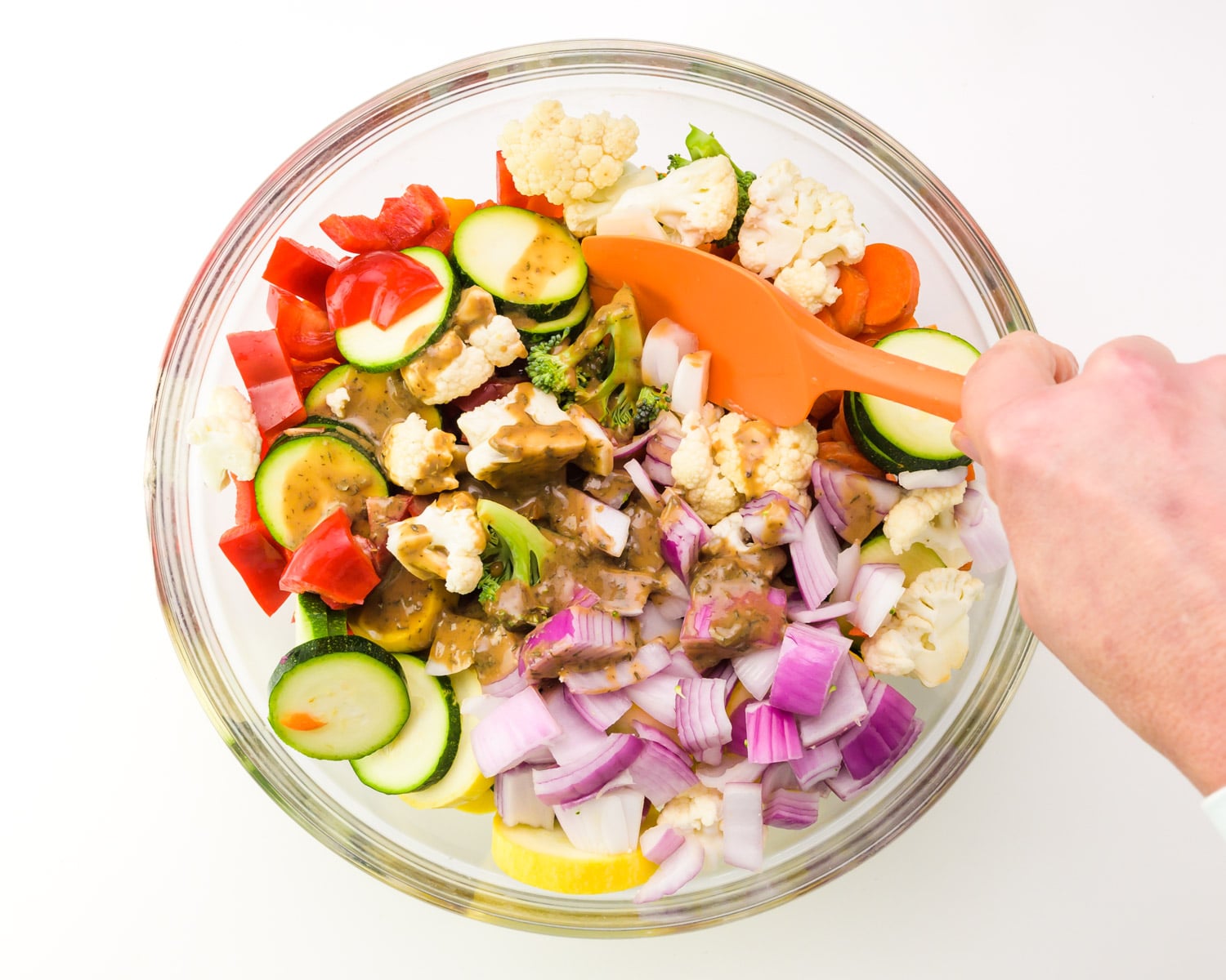 A hand holds a spatula, using it to toss vegetables in a large bowl.