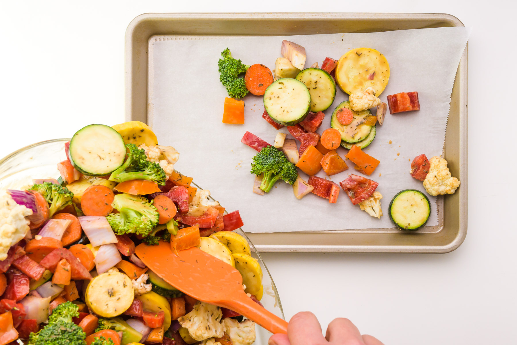 Vegetables are being poured from a bowl to a baking dish lined with parchment paper.