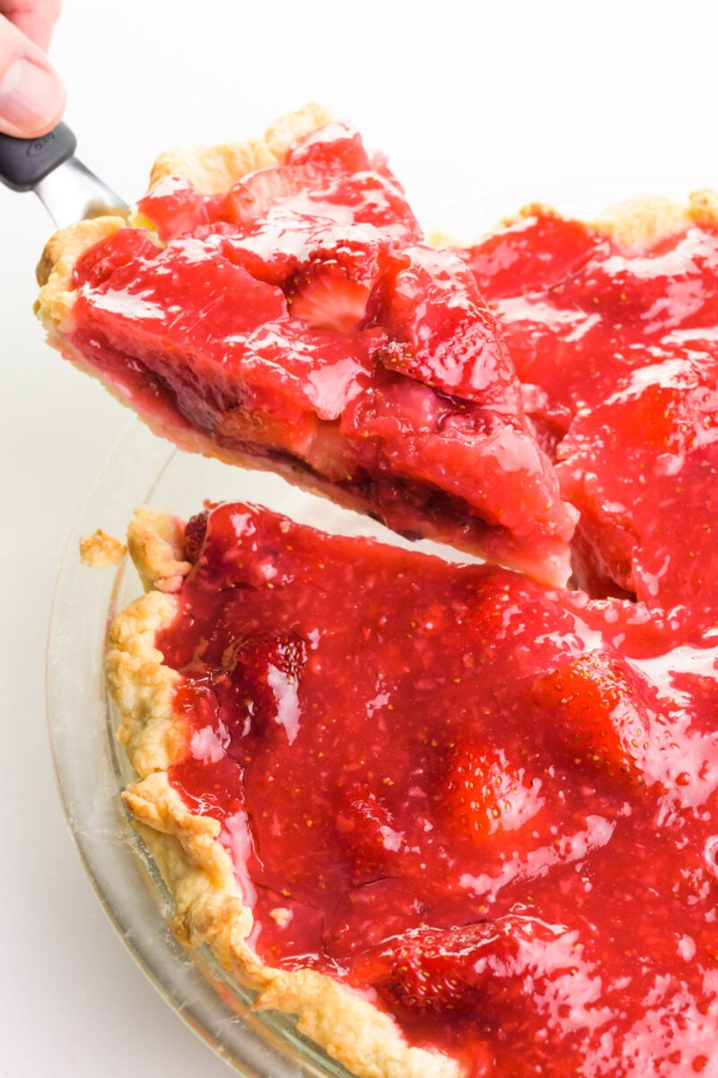 A slice of pie is being removed from a pie dish with the rest of the pie.