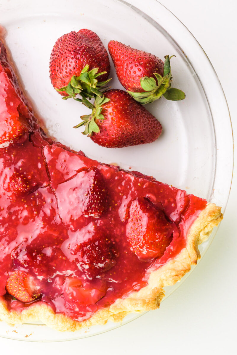 Looking down on fresh strawberries sitting in a dish where slices have been removed from a strawberry pie.