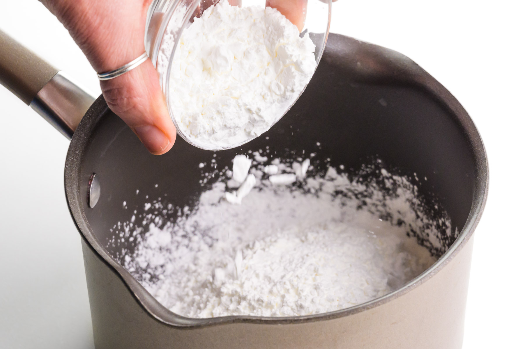 A hand holds a bowl, adding cornstarch to a saucepan.