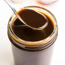 A closeup of vegan Worcestershire sauce in a spoon hovering over a mason jar full of more of the sauce.