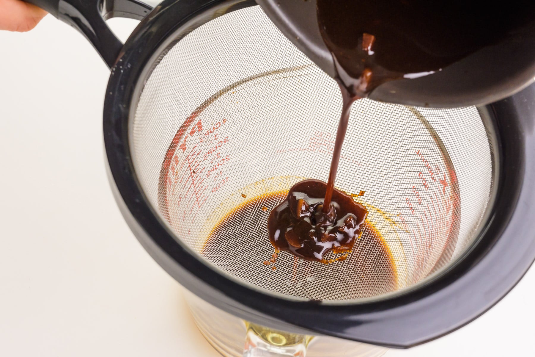 A dark sauce is being poured through a fine mesh strainer.