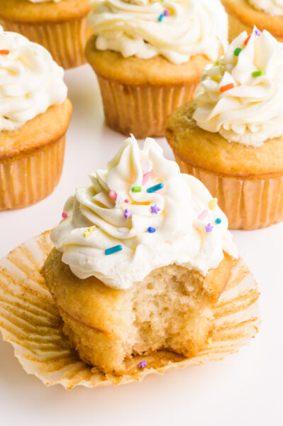 A veganized cake mix cupcake has a bite taken out. It sits in front of several other cupcakes.