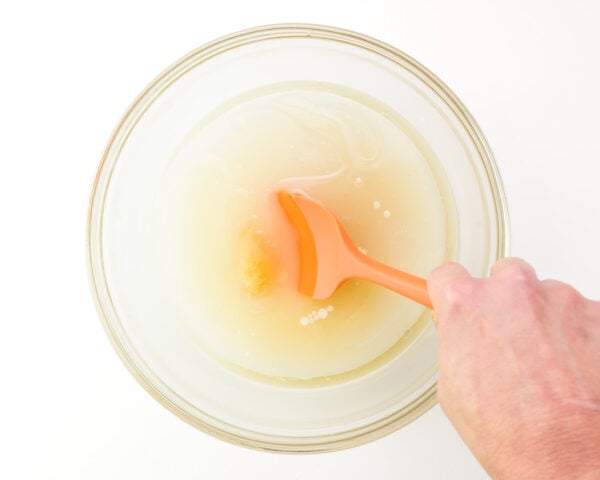 A hand holds an orange spatula, stirring together ingredients in a mixing bowl.